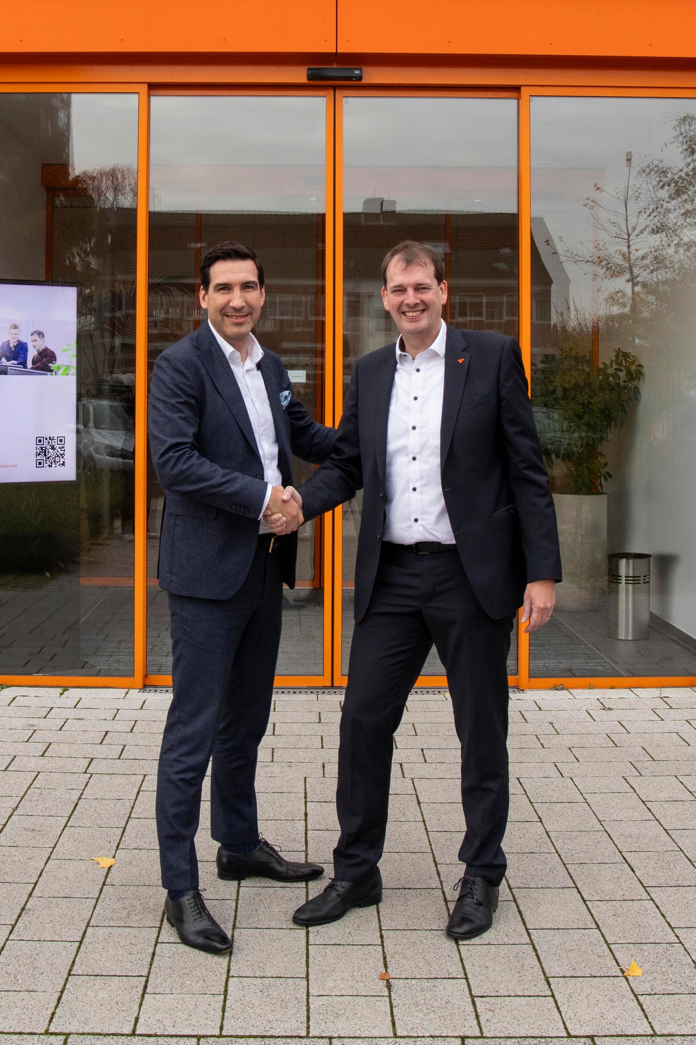 Marcus Pannier and Bernd Hillbrands shake hands in front of the entrance to the Orgadata building